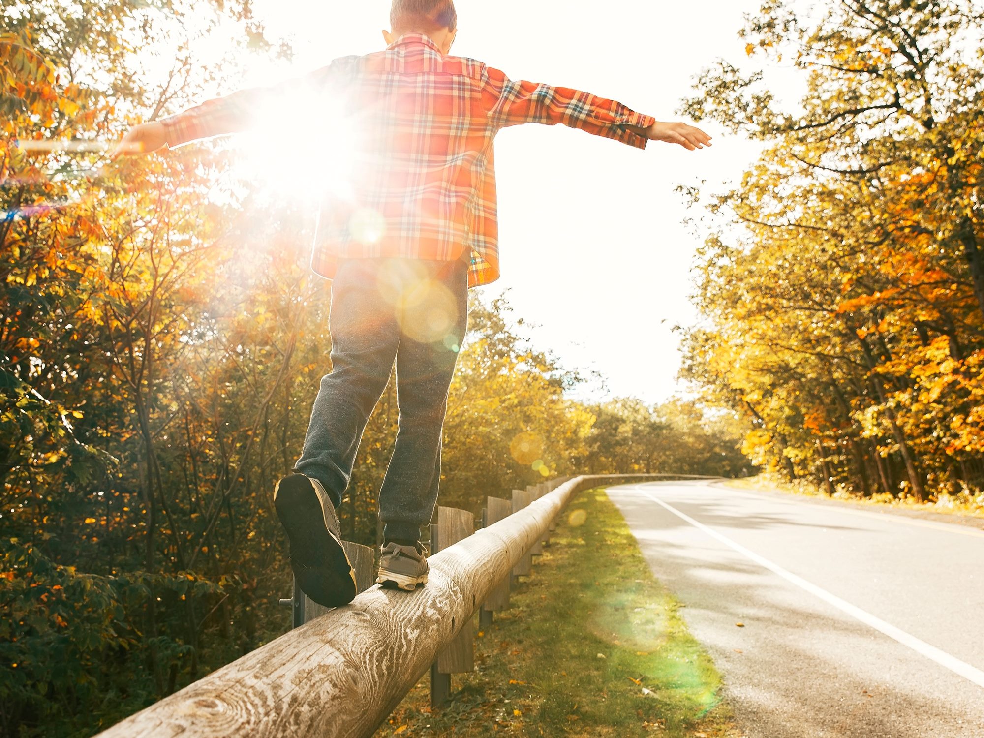 A young child walks atop a roadside fence rails keeping their balance with trees and sun in background in piece about B2B marketing strategies.