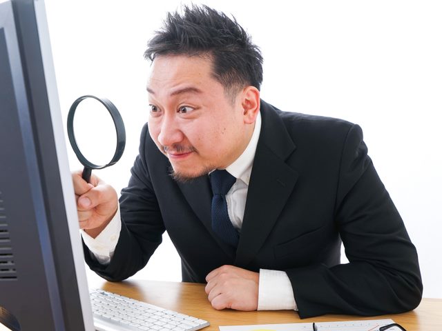 A businessman peering through a magnifying glass at his PC's monitor. CDP Evaluation Concept