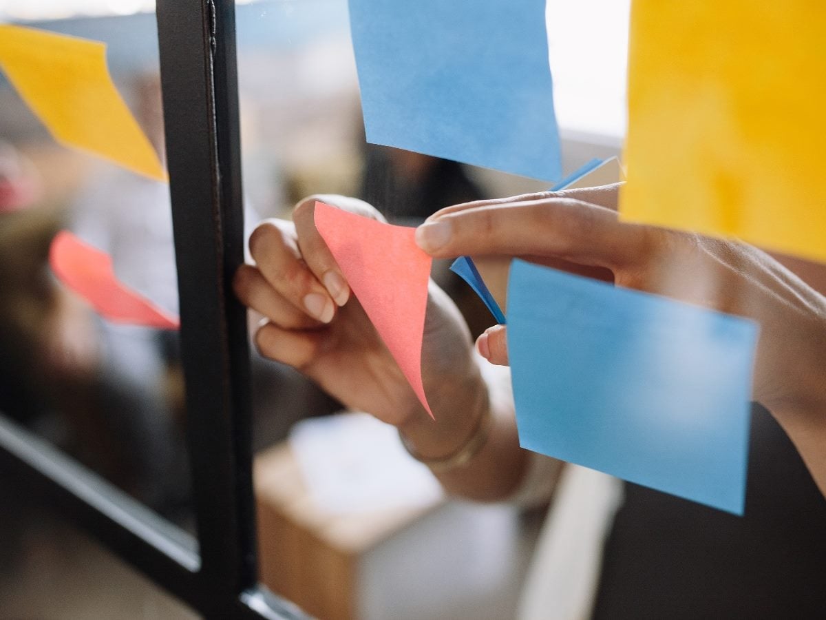 Close-up photo of hands placing colorful sticky notes on a glass wall during a customer journey mapping or collaborative strategy workshop, symbolizing CX planning, brainstorming and organizational alignment.