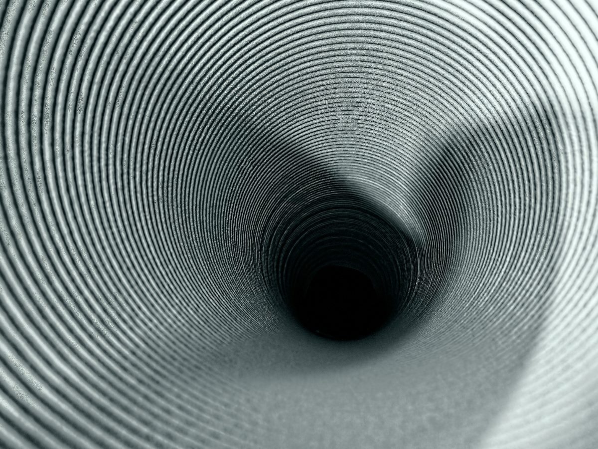Close-up view looking deep into a ribbed metal or plastic tunnel, creating a hypnotic spiral effect with shadows and highlights emphasizing the concentric texture.