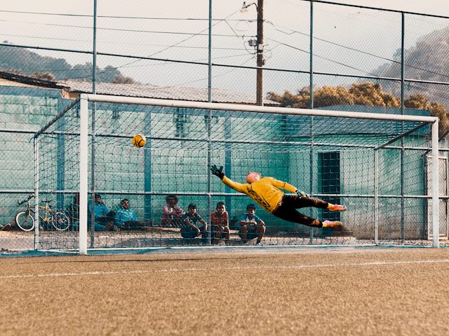 goalie leaping to stop soccer ball from getting in the goal