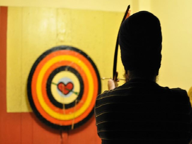 person shooting bow and arrow at target with a heart for a bullseye