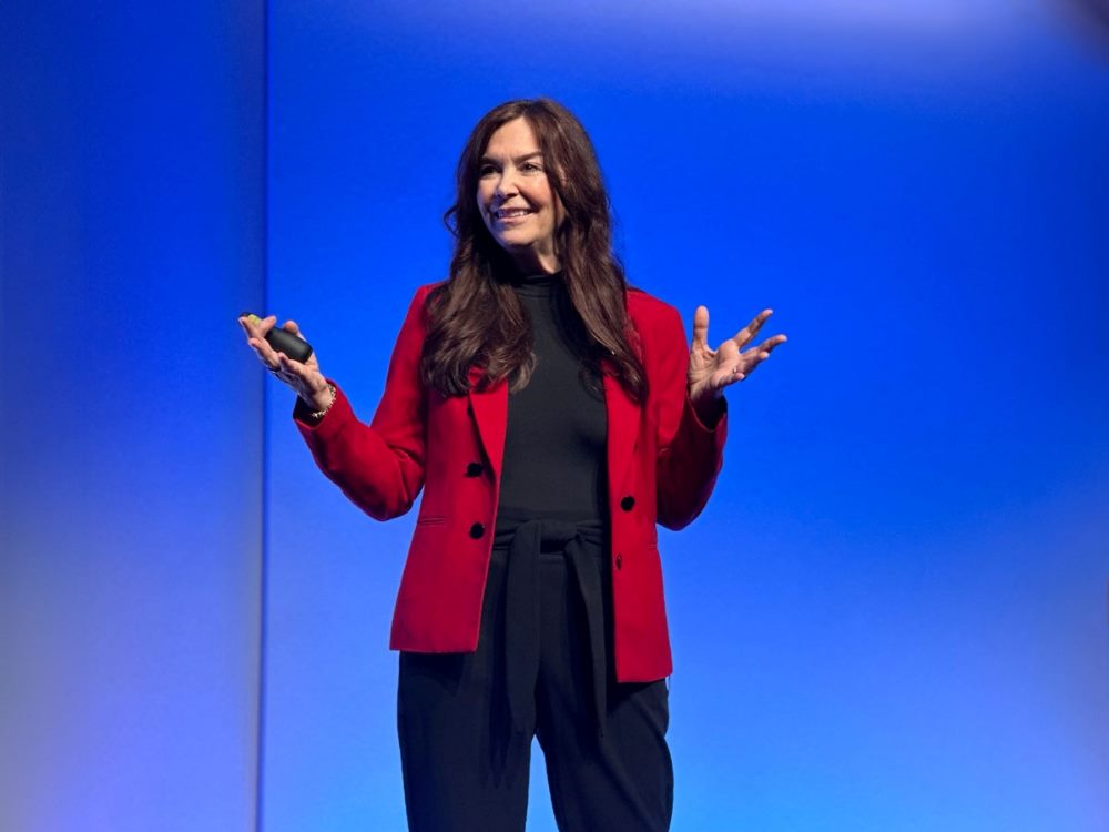 Gartner Distinguished VP Analyst Rita Sallam was a speaker at the Gartner Data & Analytics Summit wearing a red jacket and against a bright blue background.