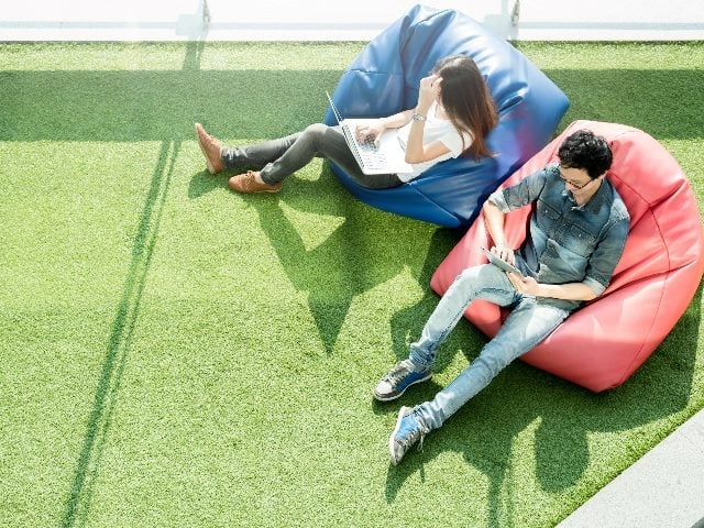 Sky-view of two people sitting on bean bags, one using a laptop and the other a tablet. 