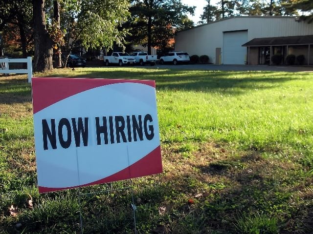 A "Now Hiring" sign on a lawn.