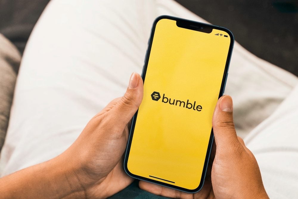 Woman holding smartphone with Bumble app displayed.