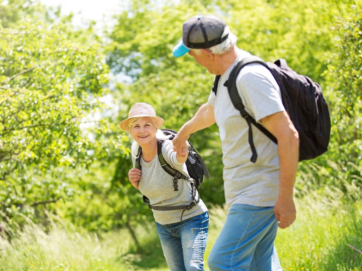 Elderly couple hiking, with the man lending hand to the woman on a hill.
