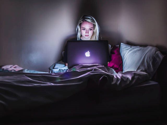 woman shopping online in the dark, lit by her laptop