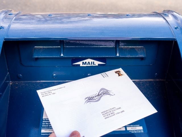 Close-up of someone's hand placing an absentee election ballot into a mailbox.