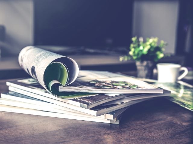 Stack of magazines on a table with a cup of coffee next to them.