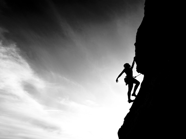 A climber is silhouetted against the evening sky as she clings to a steep rock face