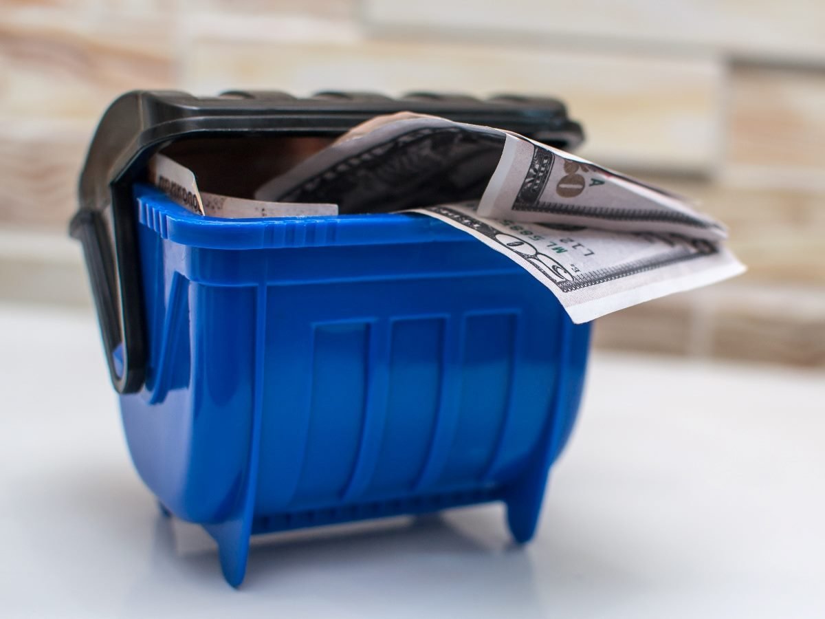 Close-up of U.S. dollar bills stuffed into a small blue trash bin, symbolizing wasted money or poor financial investment.
