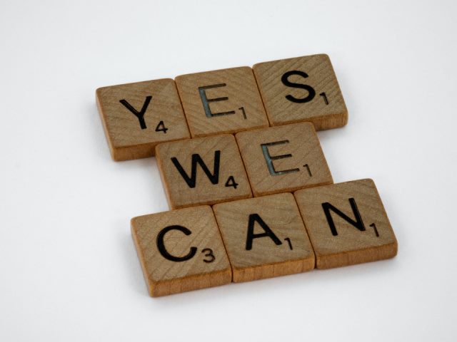 brown wooden letter tiles on a white background surface spelling the message Yes We Can
