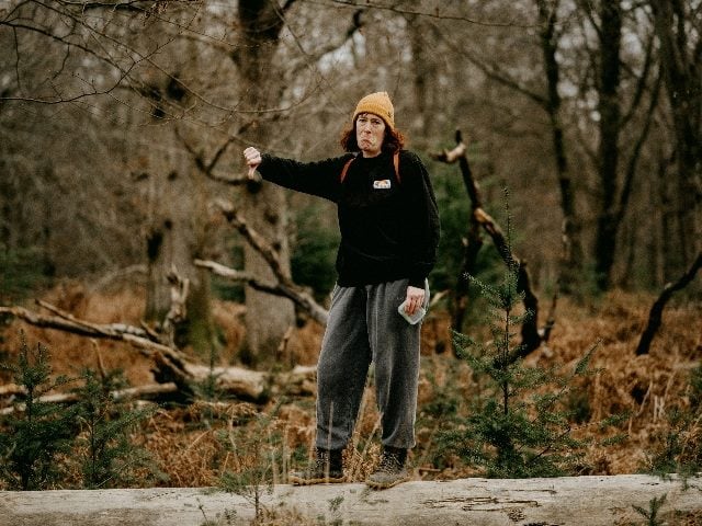 Woman in the woods in hiking gear showing a thumbs down.