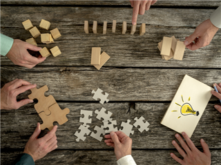 Business workers planning workplace strategy while holding puzzle pieces, creating ideas with light bulb drawn on paper and rearranging wooden blocks. - Workplace strategy