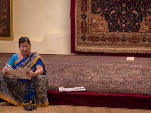woman in a sari sitting on a  platform reading  a newspaper