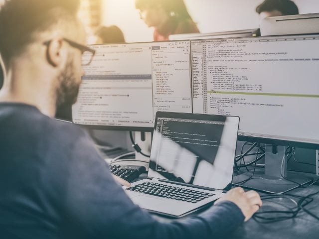 Man sitting and working on multiple computer terminals.