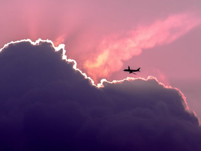 airplane flying near large cloud as sun is setting