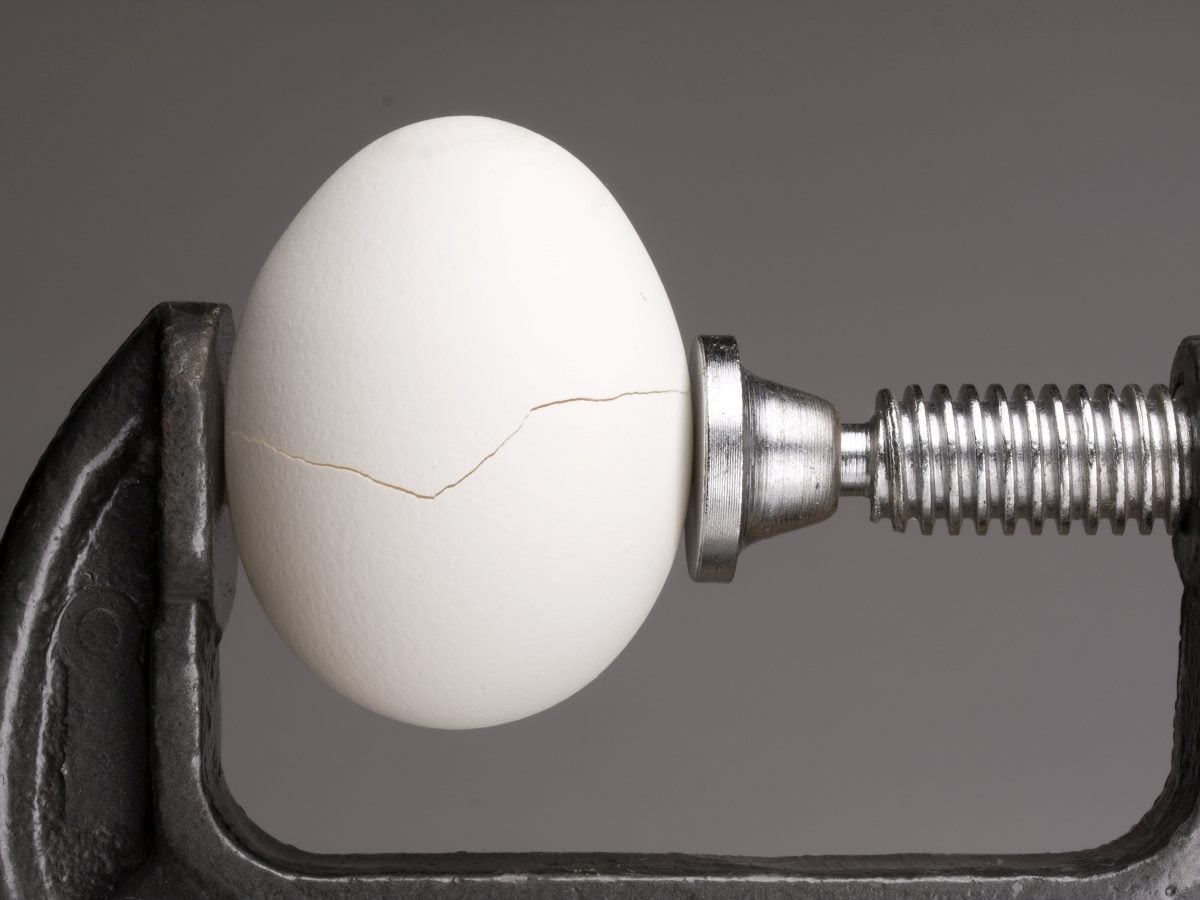 White egg cracking under pressure in a metal clamp.