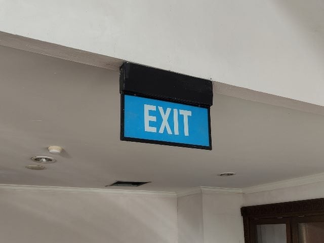 A blue and white exit sign hanging off the ceiling, representing customer support and service agents losing their jobs to generative AI.