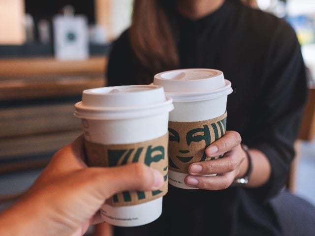 Closeup of people holding and clinking cups of coffee at Starbucks coffee shop. 