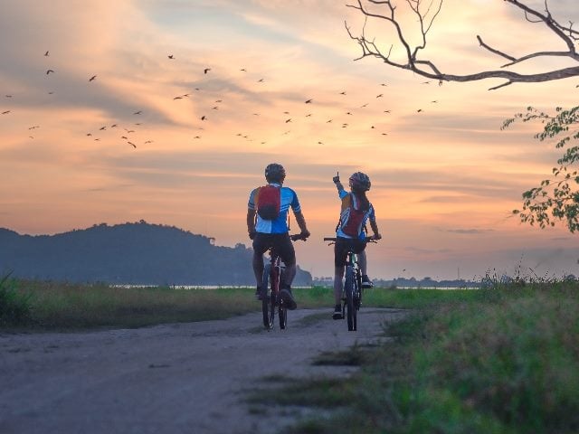 Two cyclists riding at sunset, with one pointing up to birds.