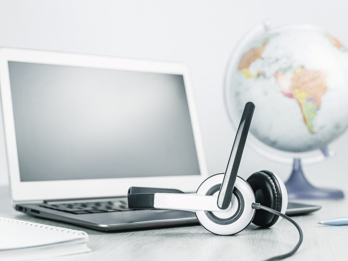 Customer service headset resting on a desk in front of an open laptop, with a globe blurred in the background. The image symbolizes contact center operations, remote customer support, AI-assisted service and global customer experience management.