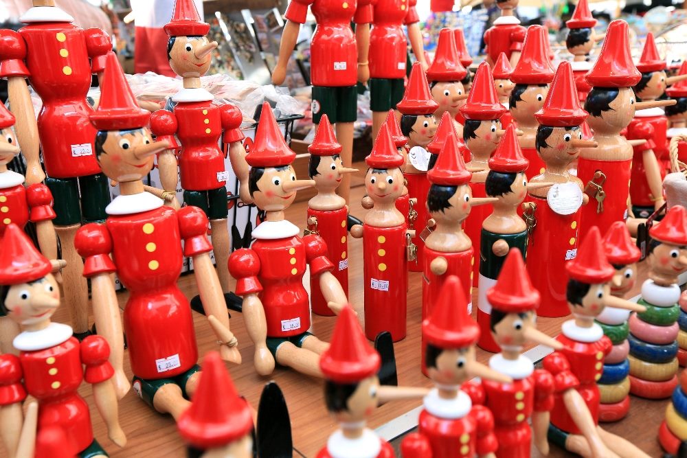 Painted wooden souvenir dolls of Pinocchio wearing red shirts with yellow buttons and red hats and black shorts in piece about AI in customer experience and misinformation.