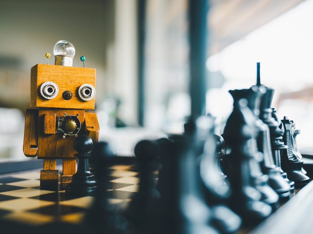 A small wooden robot stands at a chessboard, facing a row of black chess pieces, symbolizing strategic thinking and decision-making in artificial intelligence.