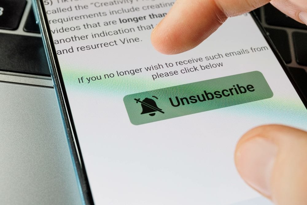 A green Unsubscribe button on smartphone screen with black text in piece about new email rules.