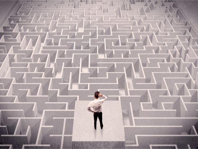 A confused businessman thinking while standing on a square platform above a detailed maze