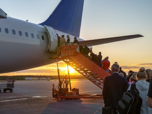 People boarding plane outside; some on the stairs to the plane, and some on the ground.