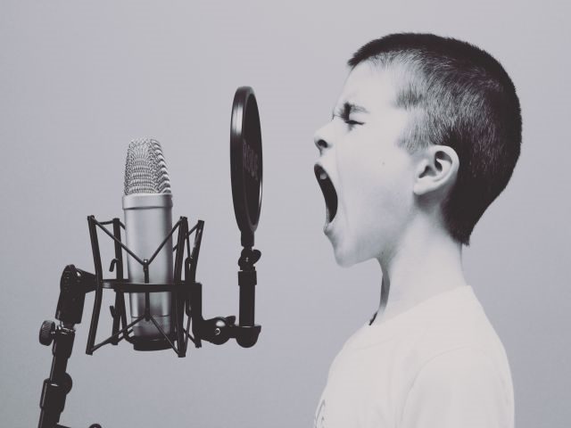 A boy singing loudly into a microphone - workplace voice technology concept