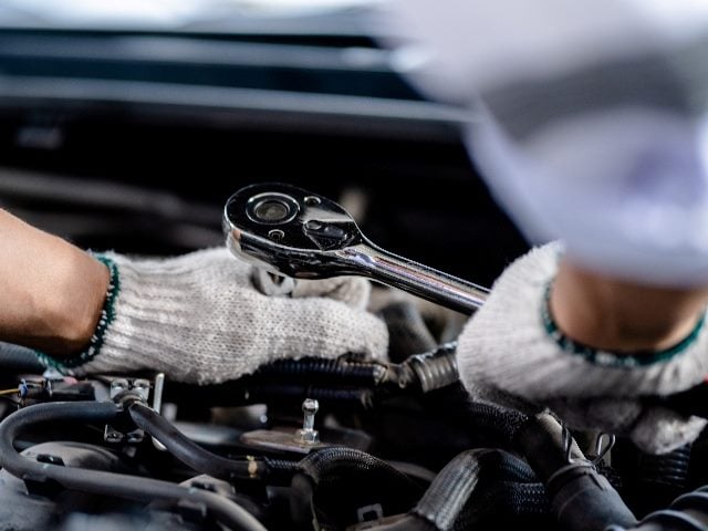 Close up of view auto mechanic repairman using a socket wrench working on engine repair. 