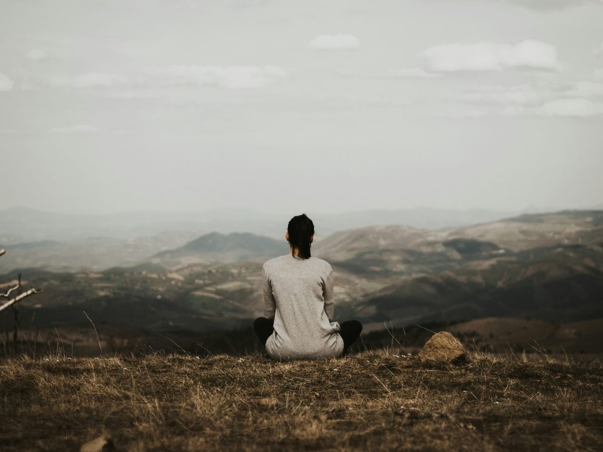 Shot from behind a woman sitting down, meditating and looking out into nature.