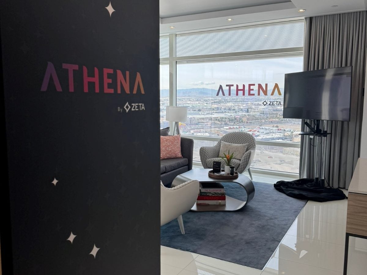 Zeta Global’s Athena marketing product branding displayed in a modern lounge-style demo space, featuring Athena logos, seating area and city skyline visible through large windows.