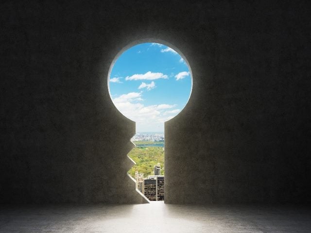 A keyhole in the concrete wall reveals a view New York City with blue sky and white clouds, symbolizing the omnichannel customer journey of the future. 