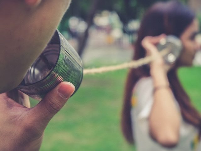 two people speaking  through a tin can telephone, attached with twine