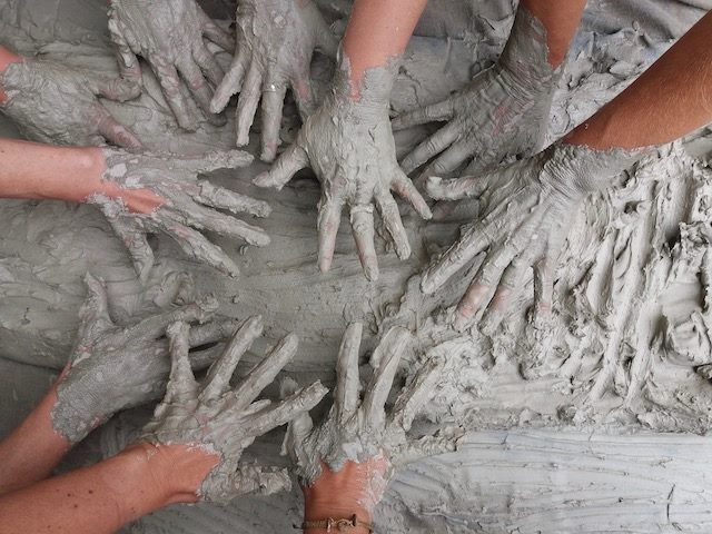 people's hands covered in clay at a pottery studio