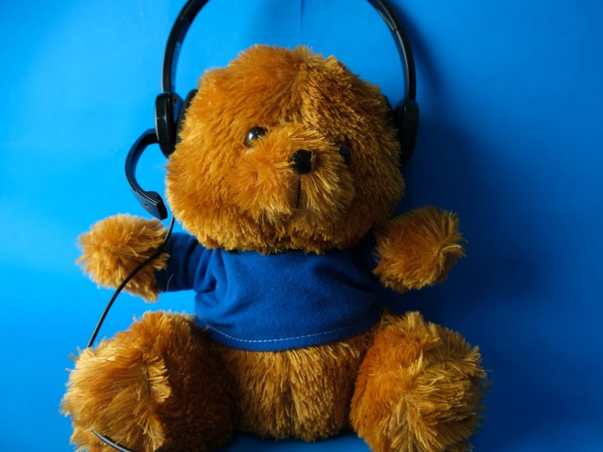 Plush teddy bear wearing a blue shirt and a call center headset, seated against a bright blue background, representing customer support or contact center service.