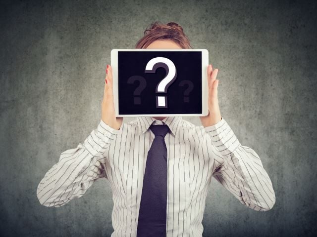 A woman in business attire holding a tablet with a question mark on the screen over her face