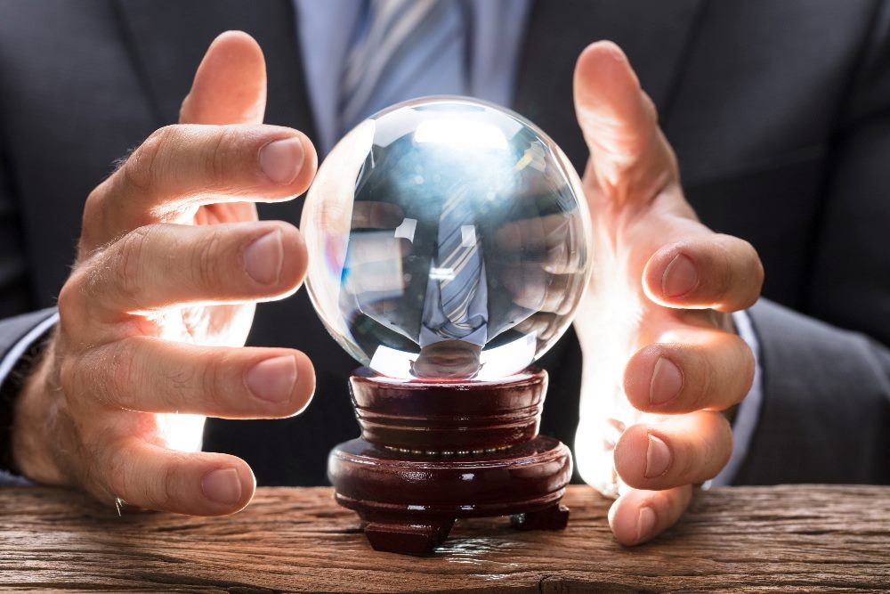 A businessperson wearing a suit jacket and tie holds their hands around a crystal ball in a piece about AI in customer experience.