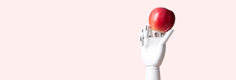 A white robotic hand, with detailed fingers and joints resembling a human hand, holds a red apple against a light pink background. The composition centers the apple delicately balanced on the robotic fingertips, symbolizing the intersection of technology and organic elements in piece about Apple and AI.