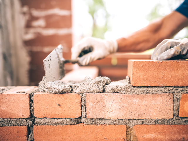 Bricklayer worker installing brick masonry on exterior wall with trowel 