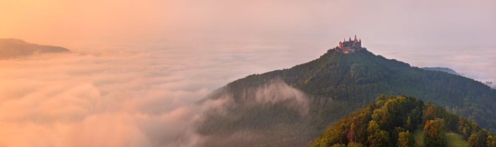 German Castle Burg Hohenzollern visible over the clouds at sunset with a golden landscape.