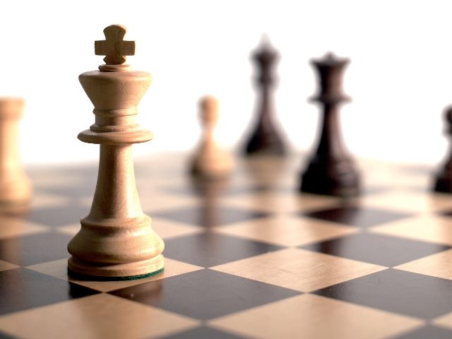 Chess pieces, with the King in the foreground, and the other pieces blurred in the background sit on chess board, indicating the importance of voice of the customer strategies. 