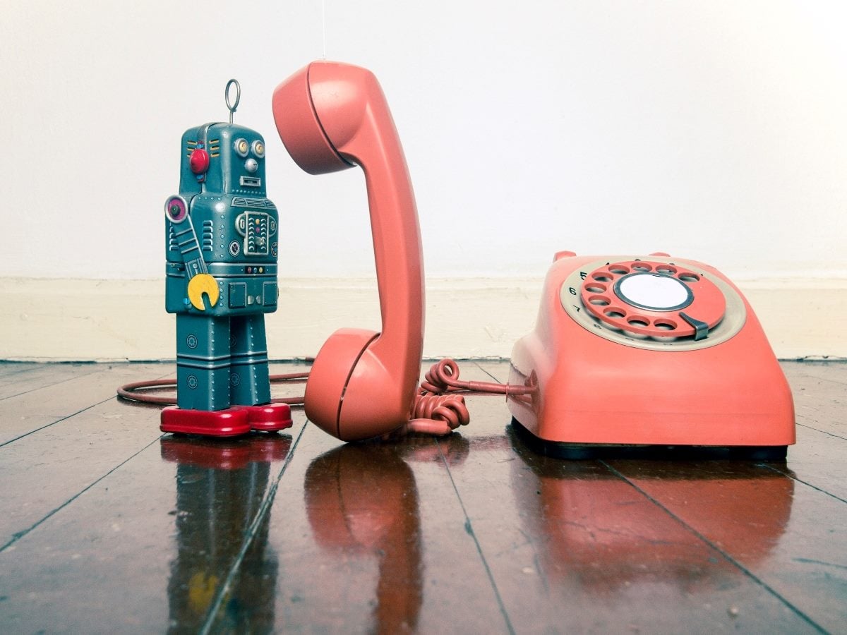 Toy robot standing next to a vintage rotary telephone, symbolizing the shift from traditional call-based systems to modern conversational AI.