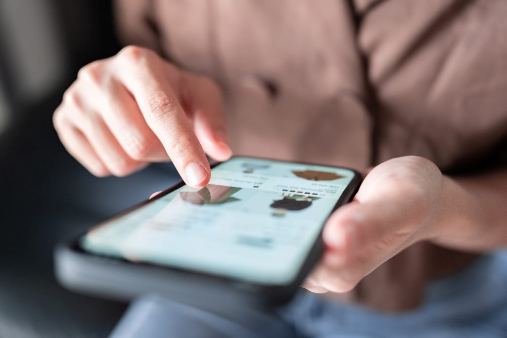 A person wearing a brown top is shopping online on a smart phone with a blurred background in piece about digital customer experience trends in 2024.