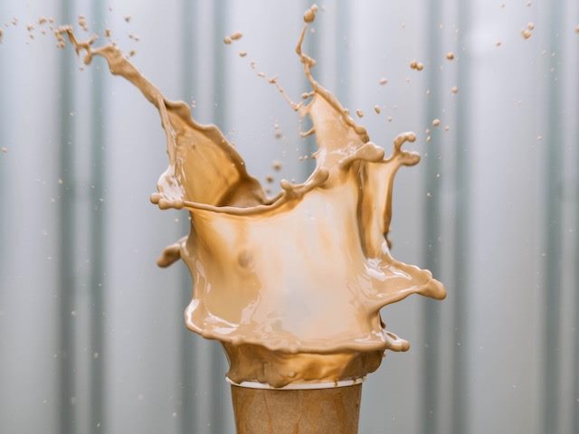 coffee spill  captured in  process, flying up  over a take  out coffee cup's rim