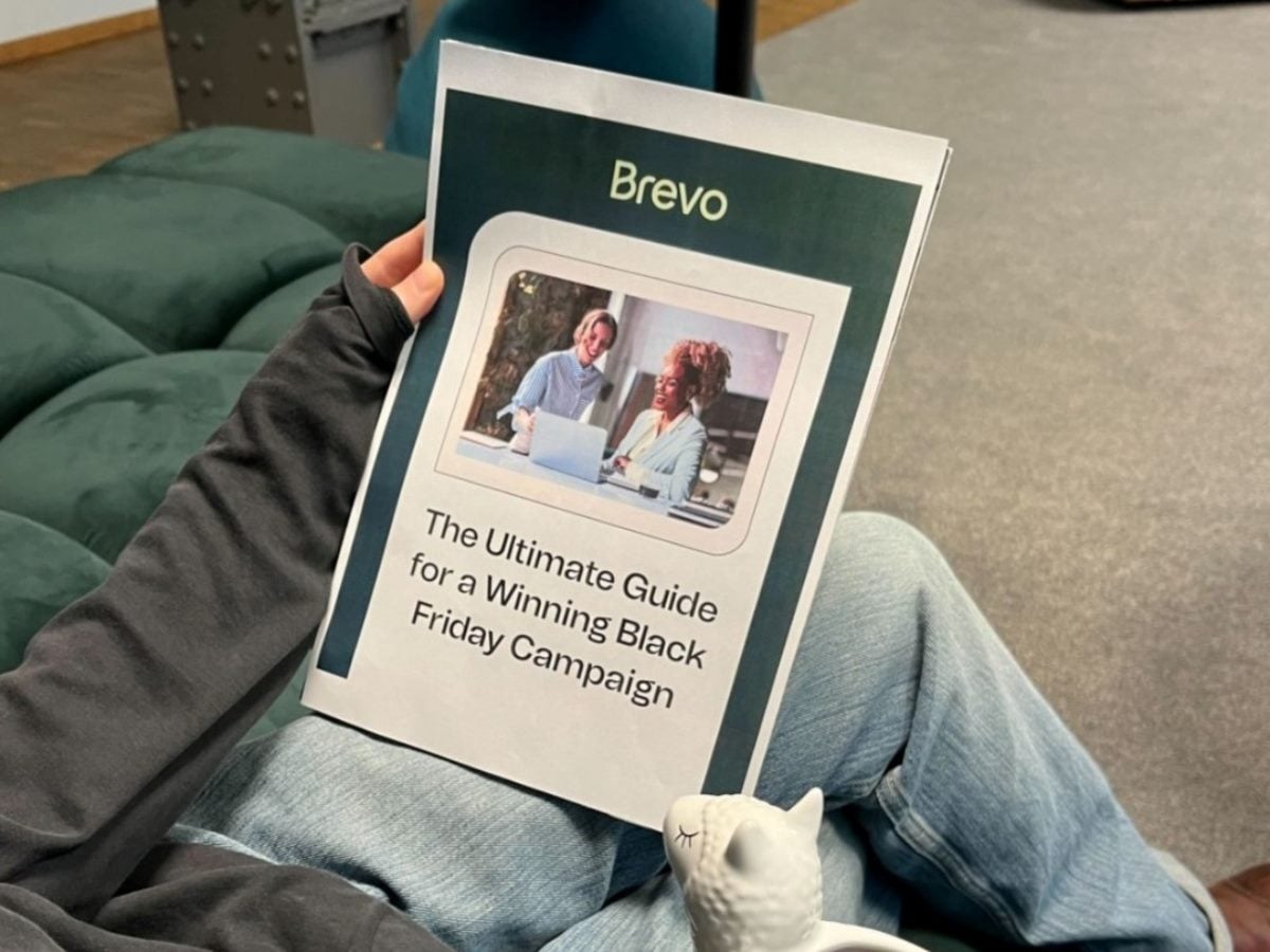 Printed Brevo guide titled “The Ultimate Guide for a Winning Black Friday Campaign,” held by a seated person in a casual office setting.